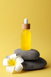Bottle of face serum, spa stones and beautiful flower on yellow background