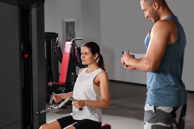 Photo of Trainer writing down plan of workouts while woman doing exercise in modern gym