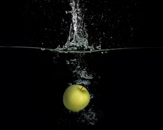 Ripe apple falling down into clear water with splashes against black background