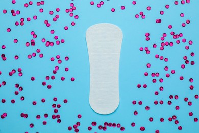 Sanitary pad and pink sequins on light blue background, flat lay. Menstrual cycle