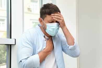Man in medical mask suffering from pain during breathing near window