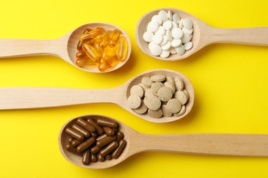 Wooden spoons with different dietary supplements on yellow background, flat lay