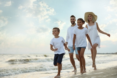 Happy family walking on sandy beach near sea at sunset