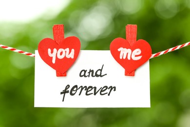 Romantic message. Card with You And Me Forever text made of paper hearts and clothespins outdoors