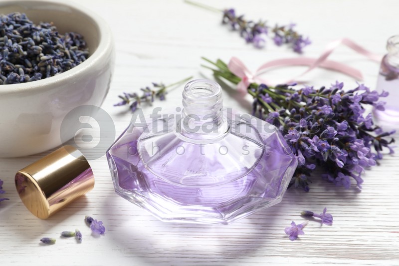 Photo of Bottle of natural perfume and lavender flowers on white wooden table. Cosmetic product