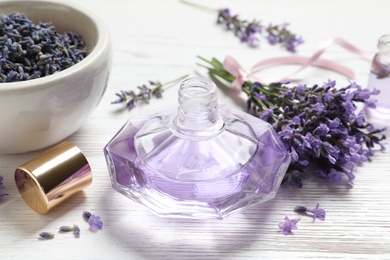 Photo of Bottle of natural perfume and lavender flowers on white wooden table. Cosmetic product