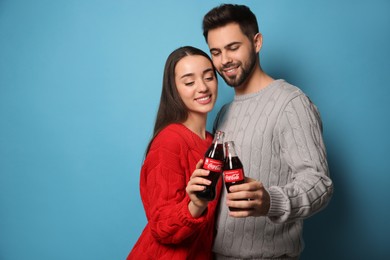 MYKOLAIV, UKRAINE - JANUARY 27, 2021: Young couple holding bottles of Coca-Cola on light blue background. Space for text