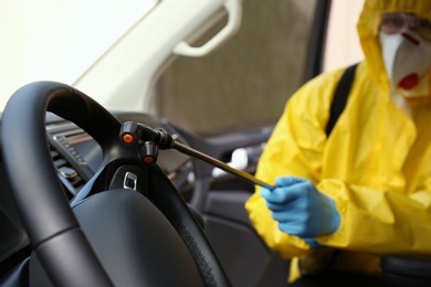 Person in protective suit disinfecting car, focus on sprayer. Preventive measure during coronavirus pandemic