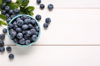 Tasty fresh blueberries and green leaves on white wooden table, flat lay. Space for text