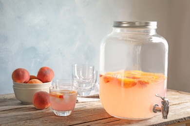 Peach cocktail in glass and jar with tap on table. Refreshing drink