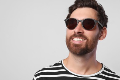 Portrait of smiling bearded man with stylish sunglasses on light grey background, closeup. Space for text