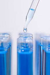 Dripping reagent into test tube with blue liquid on light background, closeup. Laboratory analysis