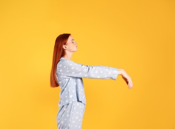 Young woman wearing pajamas in sleepwalking state on yellow background