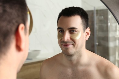 Young man with under eye patches near mirror at home