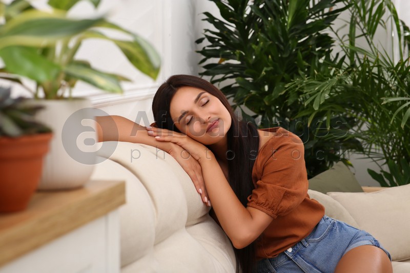 Beautiful woman sitting on sofa in living room decorated with houseplants. Interior design
