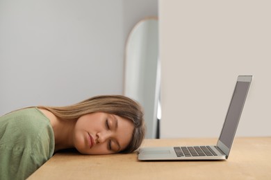 Young woman sleeping in front of laptop at wooden table indoors