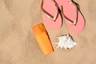 Bottle with sun protection spray, flip flops and seashell on sandy beach, flat lay. Space for text