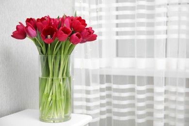 Photo of Bouquet of beautiful tulips in glass vase on white table indoors. Space for text