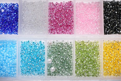 Plastic organizers with different beads as background, top view