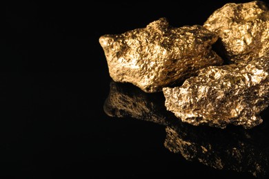 Gold nuggets on black reflective surface, space for text
