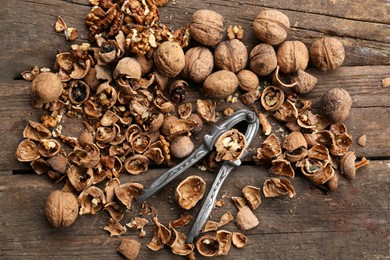 Walnuts, pieces of shells and nutcracker on wooden table, flat lay