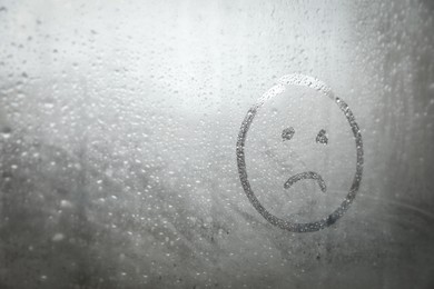 Sad face drawn on foggy window, space for text. Rainy weather