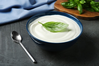 Bowl of fresh sour cream with basil and spoon on grey table
