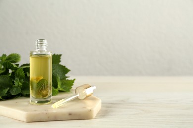 Glass bottle of nettle oil with dropper and leaves on white table, space for text