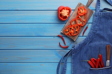Flat lay composition with denim apron and fresh peppers on light blue wooden table. Space for text