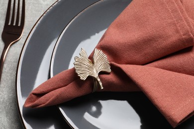 Fabric napkin and decorative ring for table setting on gray plate, closeup