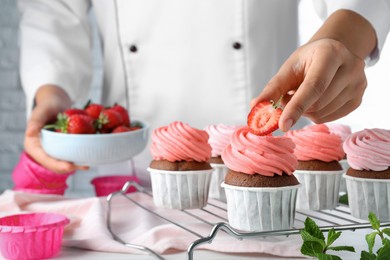 Photo of Pastry chef decorating delicious cupcakes with fresh strawberries at table, closeup
