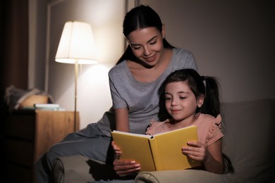 Little girl with mother reading fairy tale at home in evening