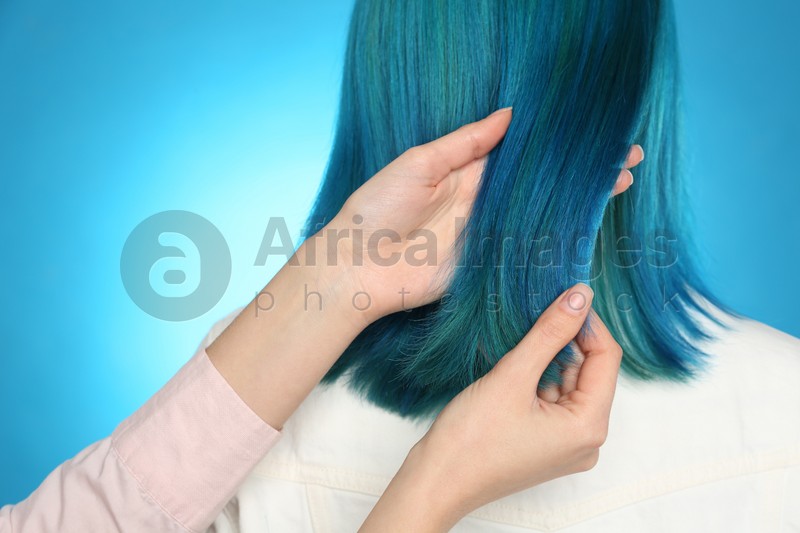 Woman with bright dyed hair on light blue background, back view
