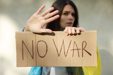 Sad woman holding poster with words No War and showing stop gesture near light wall, focus on hands