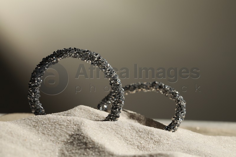 Photo of Luxury jewelry. Stylish presentation of earrings in sand against grey background, closeup