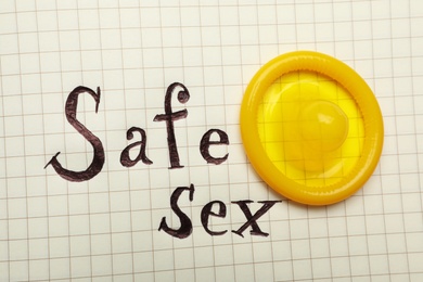 Yellow condom and words SAFE SEX on checkered paper, top view