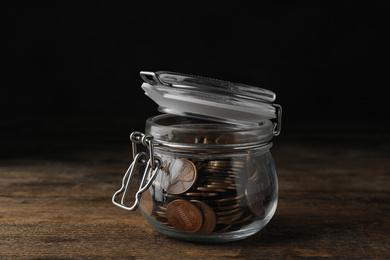 Glass jar with coins on wooden table