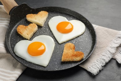 Heart shaped fried eggs and toasts in frying pan on grey table, closeup