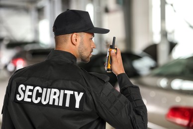 Male security guard wearing uniform using portable radio transmitter at parking