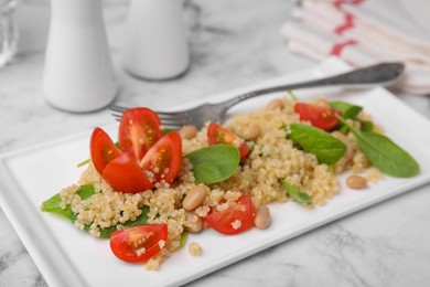 Photo of Delicious quinoa salad with tomatoes, beans and spinach leaves served on white marble table