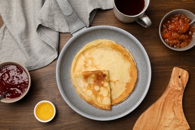 Frying pan with delicious crepes, jams, honey and aromatic tea on wooden table, flat lay