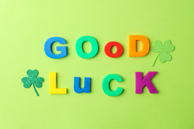Phrase GOOD LUCK made of color letters and clover leaves on green background, flat lay