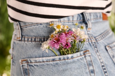 Woman with beautiful tender flowers in back pocket of jeans outdoors, closeup