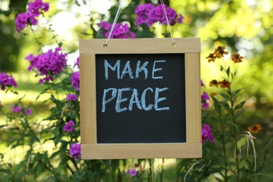 Photo of Chalkboard with phrase Make Peace near phlox flowers outdoors