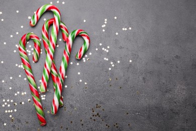 Many sweet Christmas candy canes and shiny confetti on grey background, flat lay. Space for text