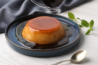 Photo of Plate of delicious caramel pudding served on white wooden table
