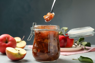 Spoon with tasty apple jam over glass jar at light table