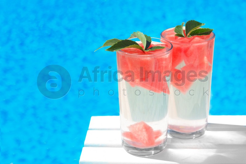 Refreshing watermelon drink in glasses near swimming pool outdoors. Space for text