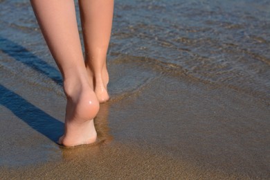 Child walking through water on seashore, closeup of legs. Space for text