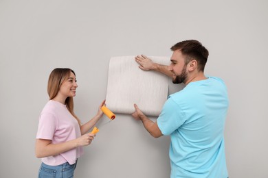 Photo of Young couple hanging new wall paper on light grey background